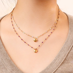 Gros plan du collier doré double couche avec perles colorées et pendentifs de cœurs