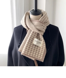 Detail of knitted houndstooth scarf showing wavy herringbone texture and woven brand label