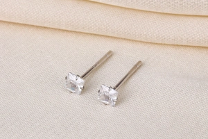 Macro shot of square-cut zircon studs in four-prong silver settings on beige fabric