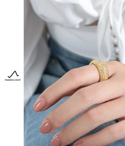 Detail of gold-plated stainless steel ring with paved crystals on a person's finger