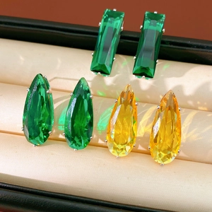 Close-up of teardrop and square zircon earrings in green and yellow crystal facets