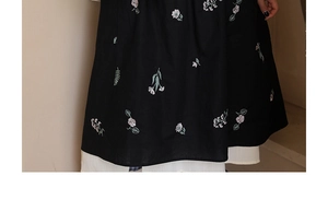 Detailed close-up of floral embroidery on black apron with white pleated lining edge