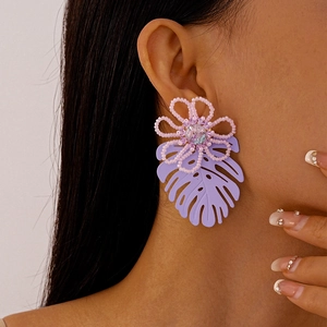 Detail of a purple handmade bead flower earring with a monstera leaf drop on model