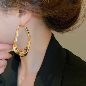 Close-up of model wearing gold irregular oversized hollow hoop earrings in a minimalist style