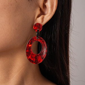 Macro shot of large red marbled resin oval hoop earrings worn by a model in soft light