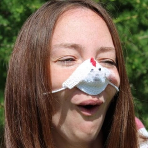 Detailed view of handmade white chicken crochet nose warmer with red comb on a person
