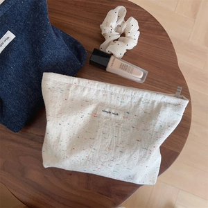 Detail of a minimalist tweed makeup bag with a 'simple wish' label on a wooden table