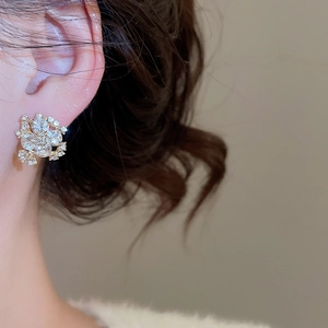 Close-up of elegant gold flower stud earrings with sparkling crystals on ear