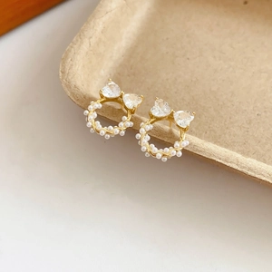 Détail macro de boucles d'oreilles nœud perle dorée avec zircone cœur sur plateau beige