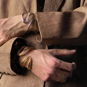 Close-up of sculptural gold and silver twisted bangle bracelets worn on model wrists