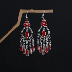 Detail of bohemian red drop earrings with intricate silver filigree on a dark branch