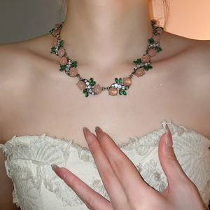 Close-up of vintage resin necklace with pink stones and green leaf accents on model