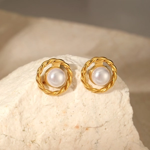 Close-up of pearl stud earrings with golden rope texture on a white stone background