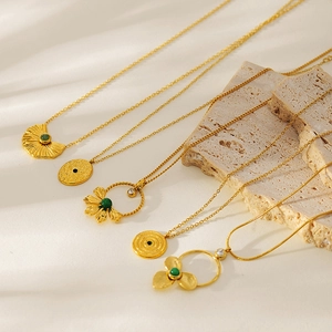 Detail of five gold-plated clover necklaces with green stones on a travertine background