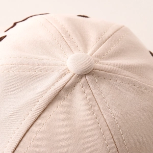 Close-up of the beige cotton baseball cap crown with double stitching and button detail