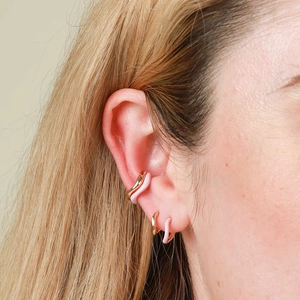 Detail view of pink and gold wavy enamel hoop earrings worn by a model in a side profile