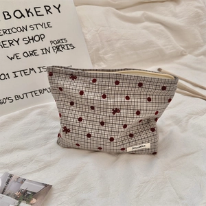 Detailed close-up of checked polka dot makeup bag with red bow embroidery and zipper