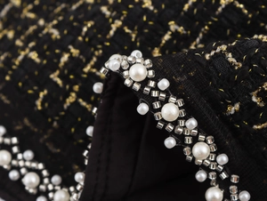 Dettaglio macro in tweed nero con fili dorati e decorazioni di perle preziose