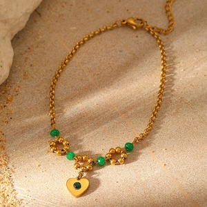Detail of gold heart charm with green stone on a natural bohemian chain bracelet