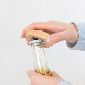 Beech wood magnetic bottle opener being used to open a glass beer bottle on white background