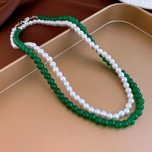 Detail of layered green beaded necklace and white pearl choker on a golden tray