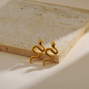 Detail of snake-shaped gold earrings placed on a beige travertine stone surface