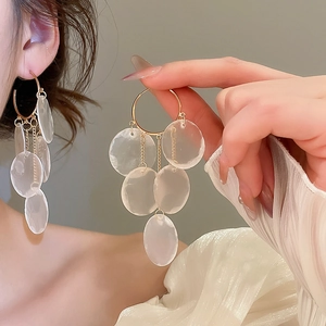 Close-up of golden hoop earrings with clear round fringe pendants worn by a model