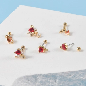Detailansicht goldener Herz-Ohrstecker mit roten Kristallen auf weißem Strukturstein