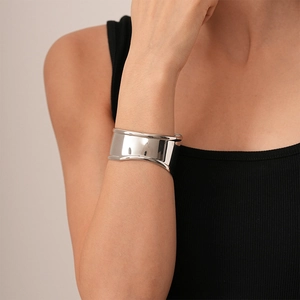 Minimalist wide silver metal cuff bracelet with sculptural asymmetric wavy edges on wrist