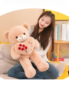 Femme asiatique tenant un grand ours en peluche beige avec un cœur brodé de roses.