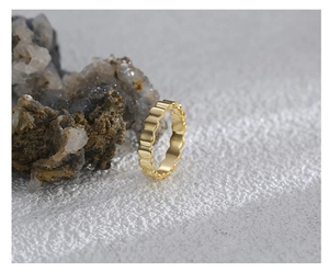 Macro detail of a minimalist gold textured wave ring on a natural stone background