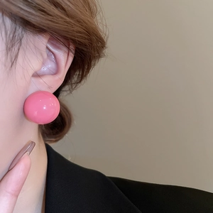 Close-up of a large glossy pink spherical stud earring on a model with a minimalist style