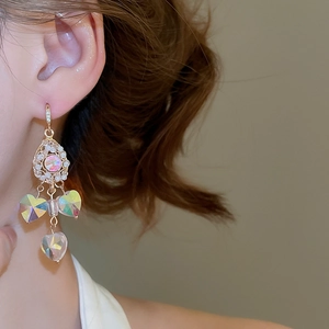 Detailed view of gold tassel earrings with colorful crystal hearts worn by a model
