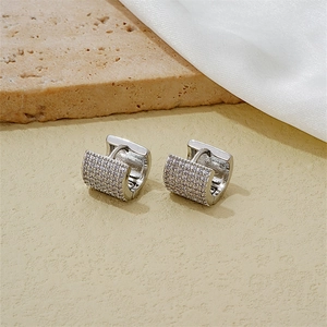 Macro shot of wide silver huggie earrings with micropave zircon on silk and stone