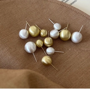 Brushed metal sphere stud earrings in gold and silver finish on textured fabric