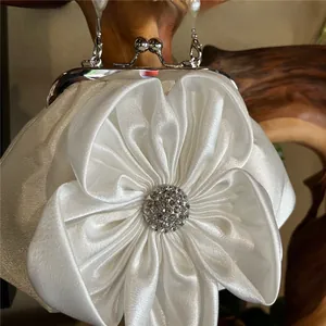 Detailed view of white silk evening clutch featuring 3D flower with rhinestone core