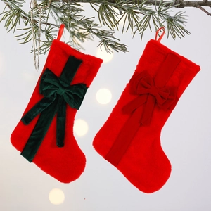 Red plush Christmas stockings with velvet bows hanging from a pine branch background