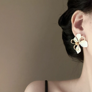 Detail view of double-layer hollow floral earrings in white and gold on a model