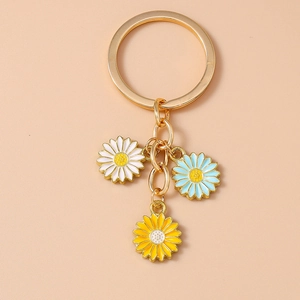 Detail of gold keychain with three colorful enamel daisy pendants in white blue and yellow
