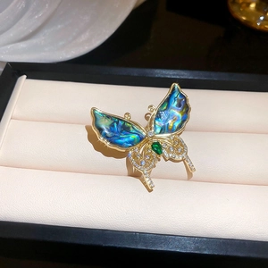 Vue macro d'une broche papillon dorée avec ailes en nacre et pierre précieuse verte