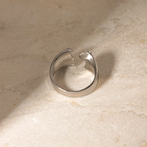 Gros plan d'une bague vague argentée sur pierre beige avec ombres naturelles