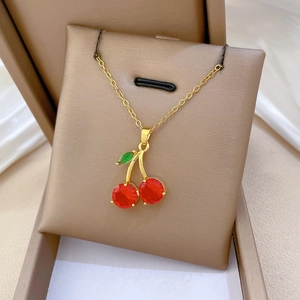 Détail d'un collier pendentif cerise doré avec cristaux rouges et feuilles vertes