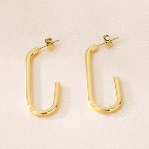 Vue détaillée des boucles d'oreilles géométriques en U dorées sur fond de soie beige