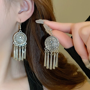 Detail of silver ethnic drop earrings with flower engraving and sleek metallic tassels