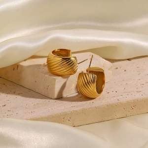 Elegant gold C-shaped textured earrings displayed on a beige stone with silk background