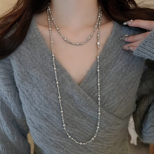 Vue détaillée d'un collier long en perles argentées irrégulières sur un pull gris