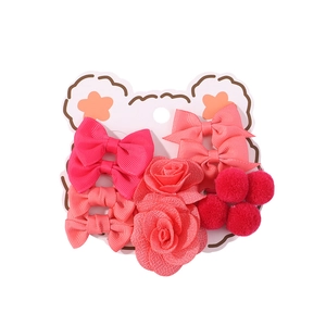 Dettaglio set di accessori per capelli bimba con fiocchi rosa e pon-pon rossi su carta