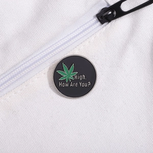 Detail of round black enamel pin featuring a green leaf and High How Are You text