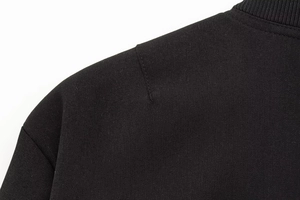 Makro-Detail der schwarzen Jacke mit Köpergewebe und geripptem Strickkragen