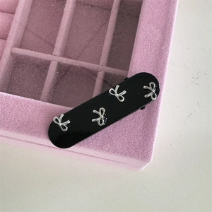 Detail of a black hair clip with four silver metal bows on a pink velvet jewelry box